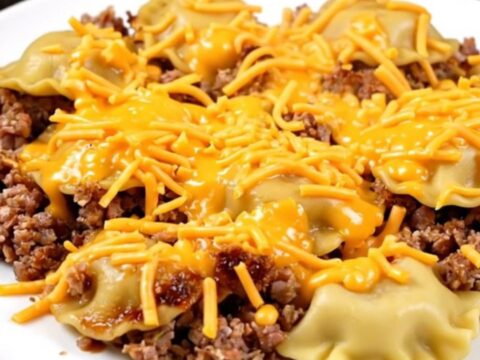 A close-up of a steaming cheesy pierogi and beef casserole served on a white plate.