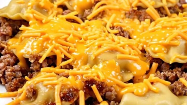 A close-up of a steaming cheesy pierogi and beef casserole served on a white plate.