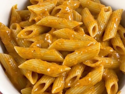 A top-down view of a slow cooker filled with penne pasta, sliced smoked sausage, and cubed cream cheese before cooking.