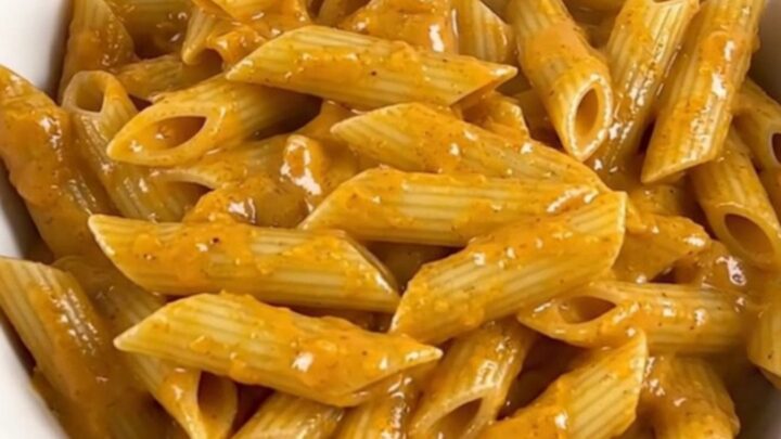 A top-down view of a slow cooker filled with penne pasta, sliced smoked sausage, and cubed cream cheese before cooking.