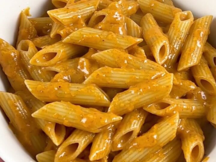 A top-down view of a slow cooker filled with penne pasta, sliced smoked sausage, and cubed cream cheese before cooking.