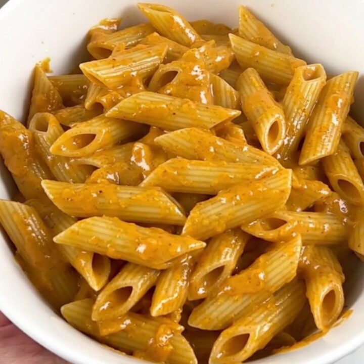 A top-down view of a slow cooker filled with penne pasta, sliced smoked sausage, and cubed cream cheese before cooking.