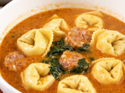 A white bowl filled with creamy spinach tortellini tomato soup, featuring visible sausage and green spinach leaves.