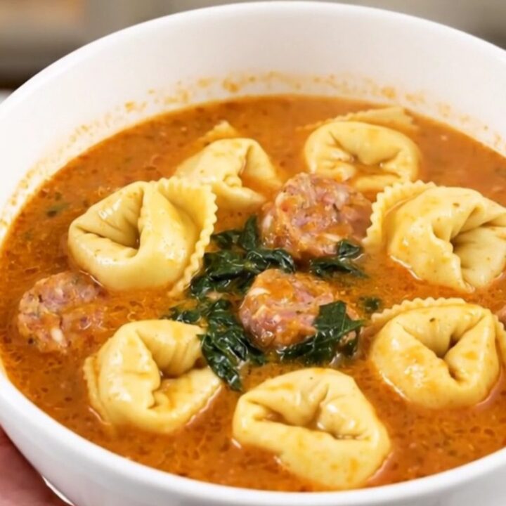 A white bowl filled with creamy spinach tortellini tomato soup, featuring visible sausage and green spinach leaves.