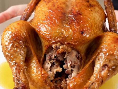 A whole Greek herb roasted chicken served on a white plate, glistening and steaming.