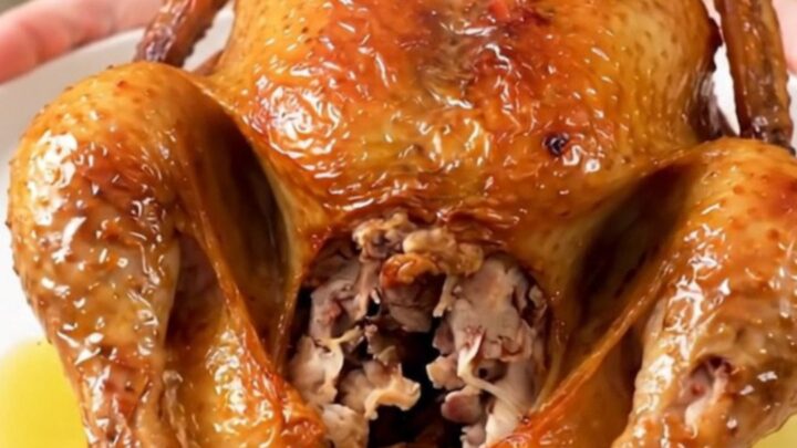 A whole Greek herb roasted chicken served on a white plate, glistening and steaming.