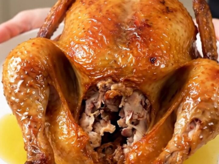 A whole Greek herb roasted chicken served on a white plate, glistening and steaming.