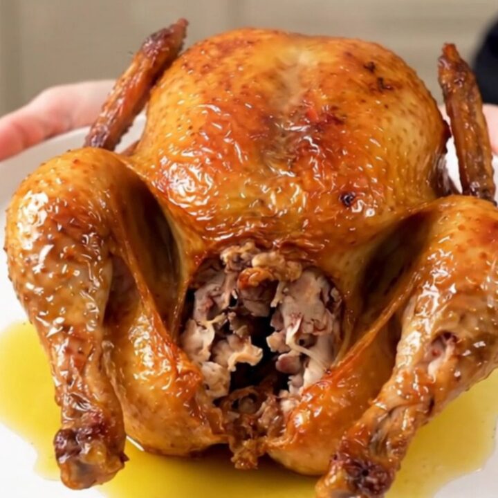 A whole Greek herb roasted chicken served on a white plate, glistening and steaming.