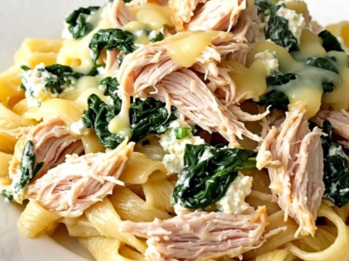 A slow cooker filled with creamy spinach ricotta chicken garnished with fresh herbs on a quartz countertop.