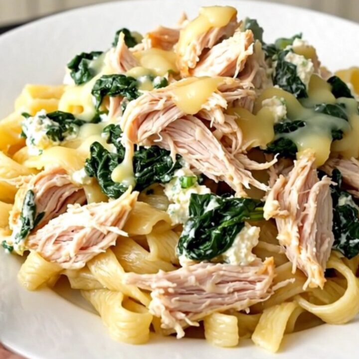 A slow cooker filled with creamy spinach ricotta chicken garnished with fresh herbs on a quartz countertop.