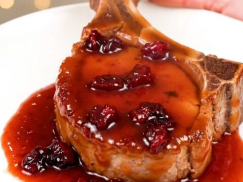 A close-up view of tender, glazed pork chops topped with dried cranberries in a slow cooker.