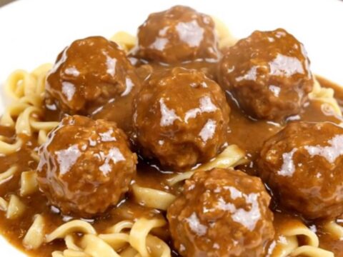 A top-down view of a black slow cooker filled with meatballs, sliced mushrooms, and cream cheese cubes.