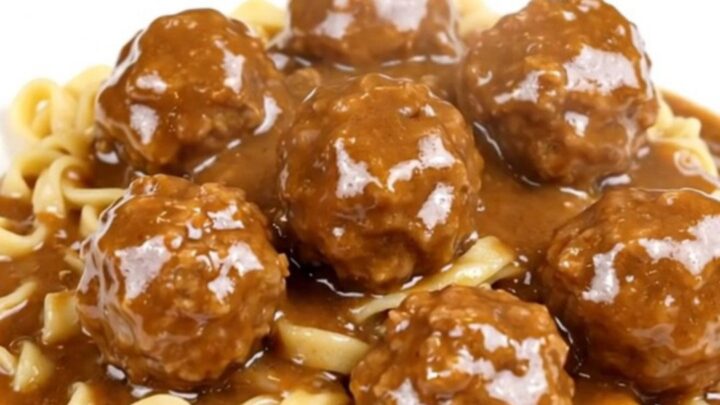 A top-down view of a black slow cooker filled with meatballs, sliced mushrooms, and cream cheese cubes.