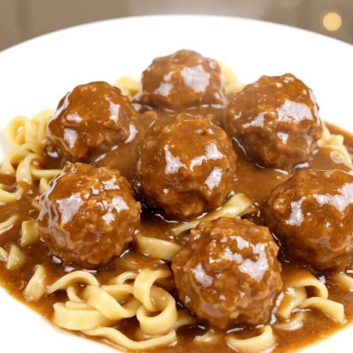 A top-down view of a black slow cooker filled with meatballs, sliced mushrooms, and cream cheese cubes.