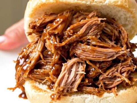 A close-up of a generous portion of shredded pulled pork piled high on a soft bun, showing glossy sauce and tender meat.
