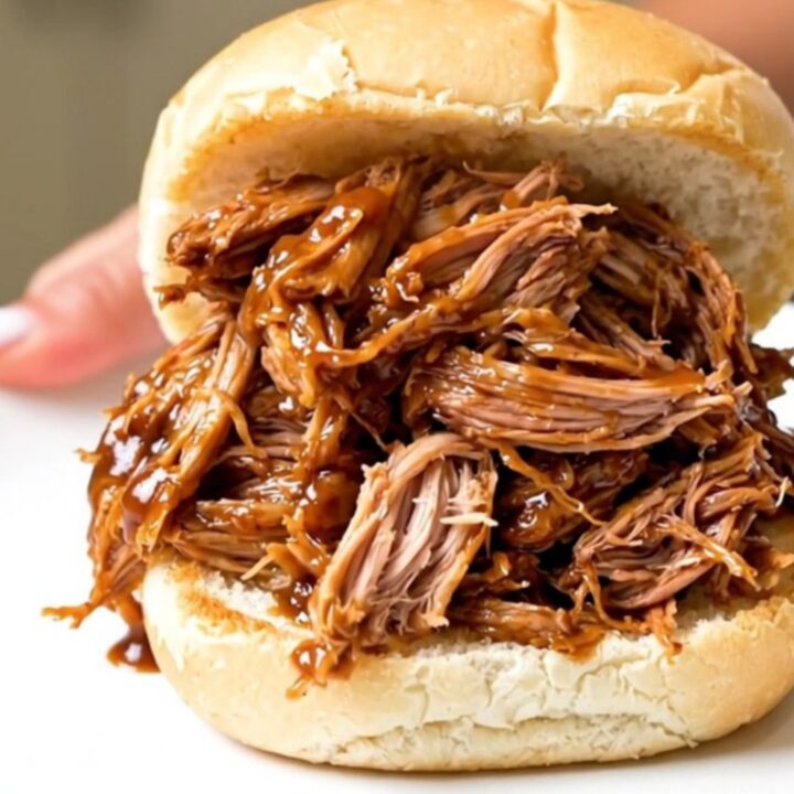 A close-up of a generous portion of shredded pulled pork piled high on a soft bun, showing glossy sauce and tender meat.