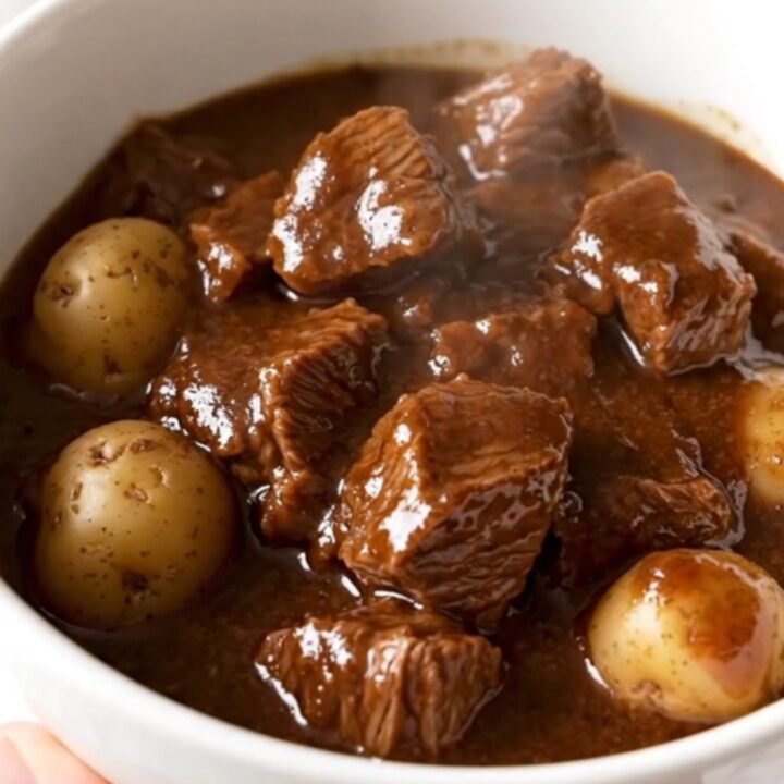 A white bowl filled with tender balsamic beef and soft potatoes in a rich, glossy dark sauce.