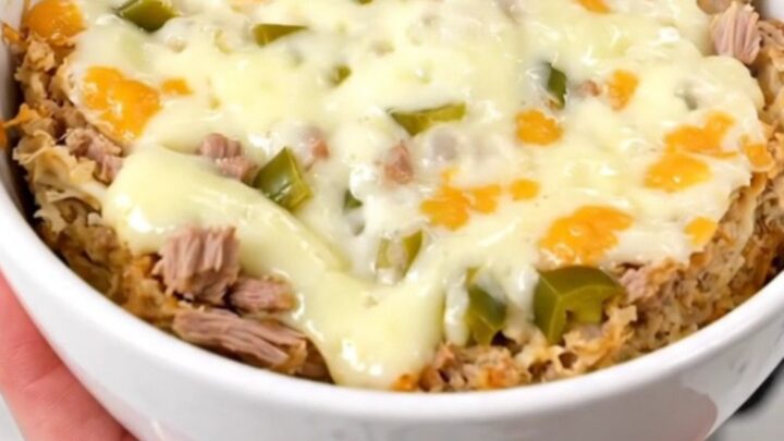 A top-down view of a creamy pulled pork dip in a slow cooker topped with melted cheese and green chiles.