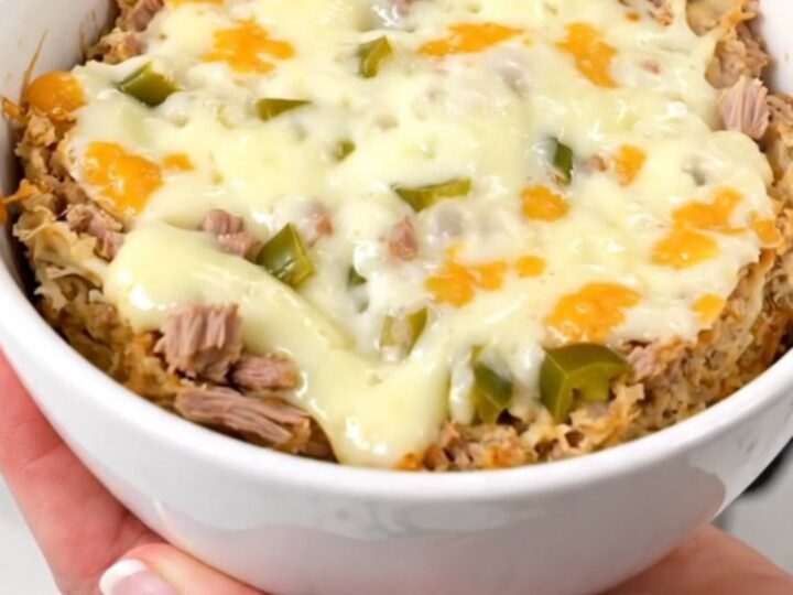 A top-down view of a creamy pulled pork dip in a slow cooker topped with melted cheese and green chiles.
