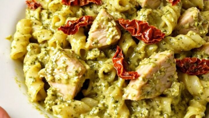 A steaming, creamy pesto chicken dish served on a white plate, showcasing the rich sauce and tender shredded chicken pieces.