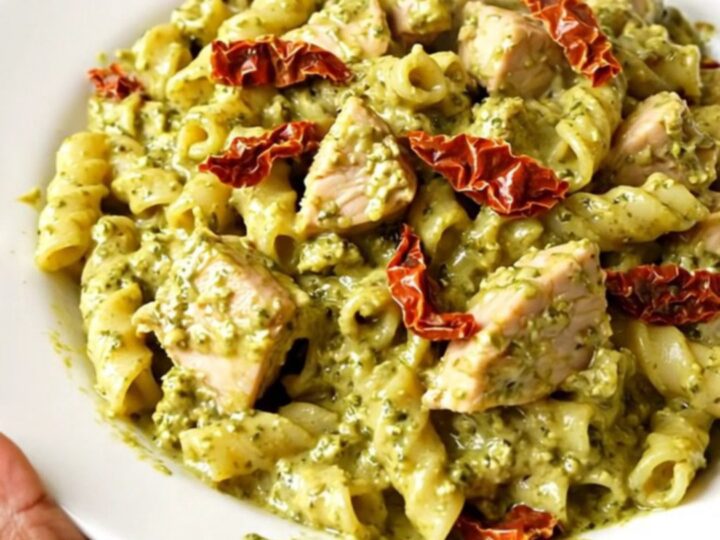 A steaming, creamy pesto chicken dish served on a white plate, showcasing the rich sauce and tender shredded chicken pieces.