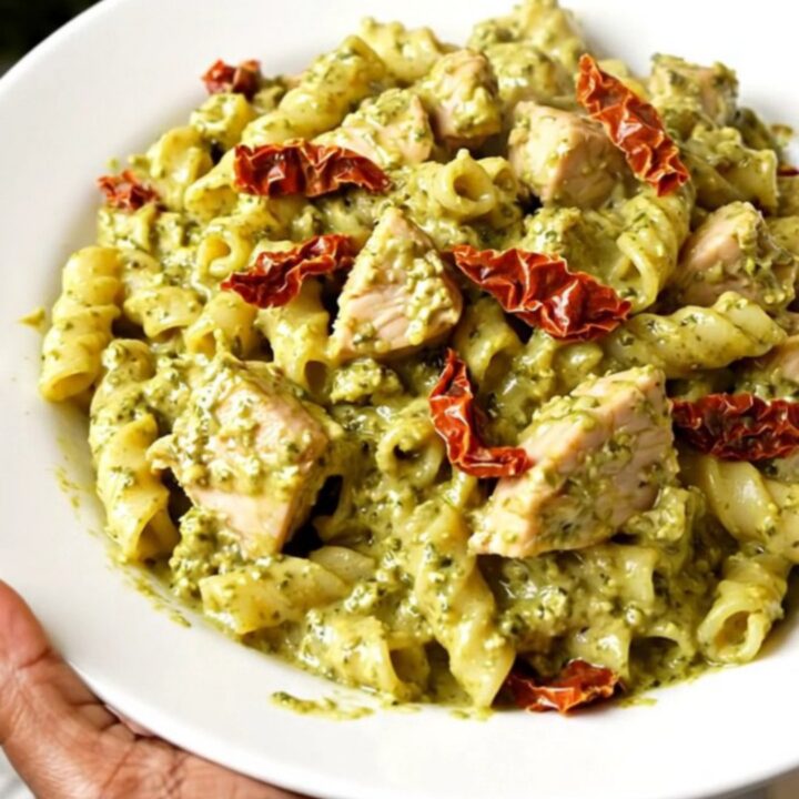 A steaming, creamy pesto chicken dish served on a white plate, showcasing the rich sauce and tender shredded chicken pieces.