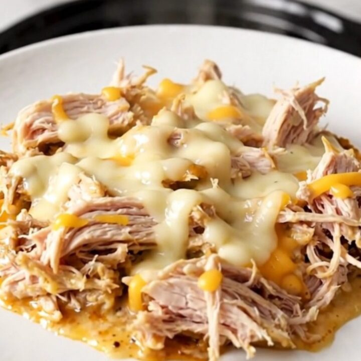 A close-up view of creamy shredded chicken with melted white cheddar in a slow cooker.