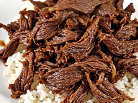 A close-up of tender, glistening shredded beef served over a mound of white rice in a white bowl.