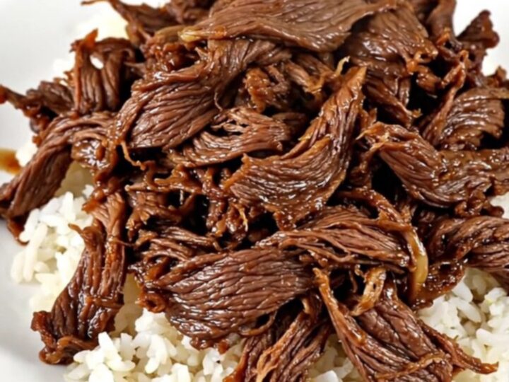 A close-up of tender, glistening shredded beef served over a mound of white rice in a white bowl.