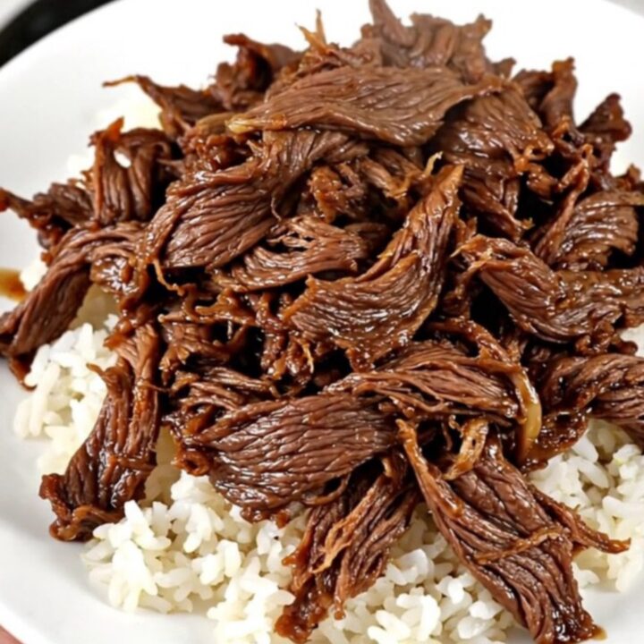 A close-up of tender, glistening shredded beef served over a mound of white rice in a white bowl.