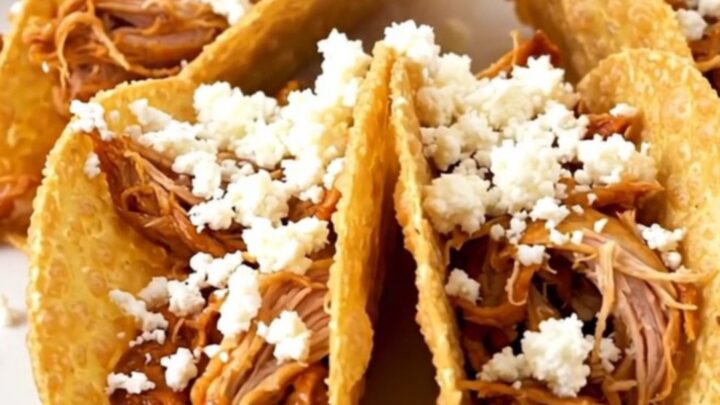 A close-up of shredded honey lime chicken in a crispy taco shell topped with crumbled white cotija cheese.