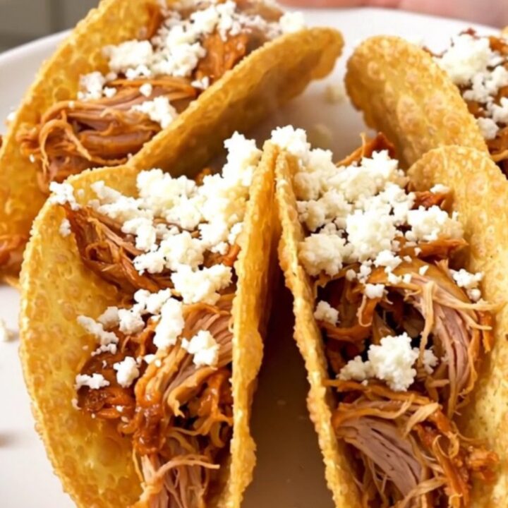 A close-up of shredded honey lime chicken in a crispy taco shell topped with crumbled white cotija cheese.