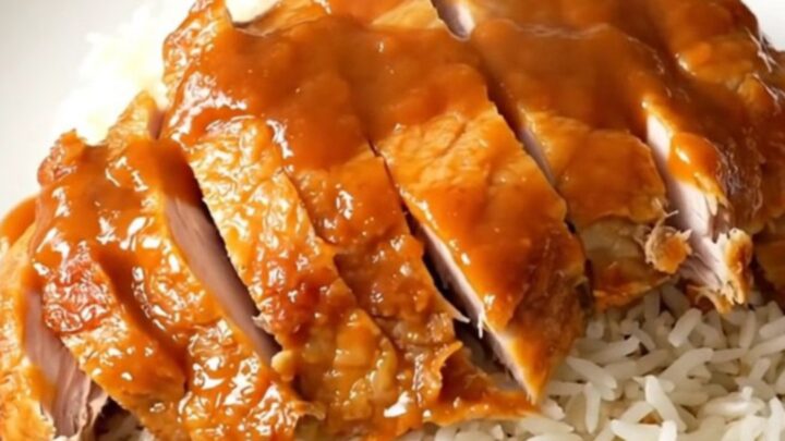 A plate of tender Chinese lemon chicken with a glossy sauce served over white rice.