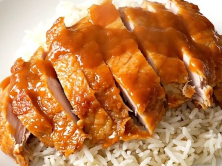 A plate of tender Chinese lemon chicken with a glossy sauce served over white rice.