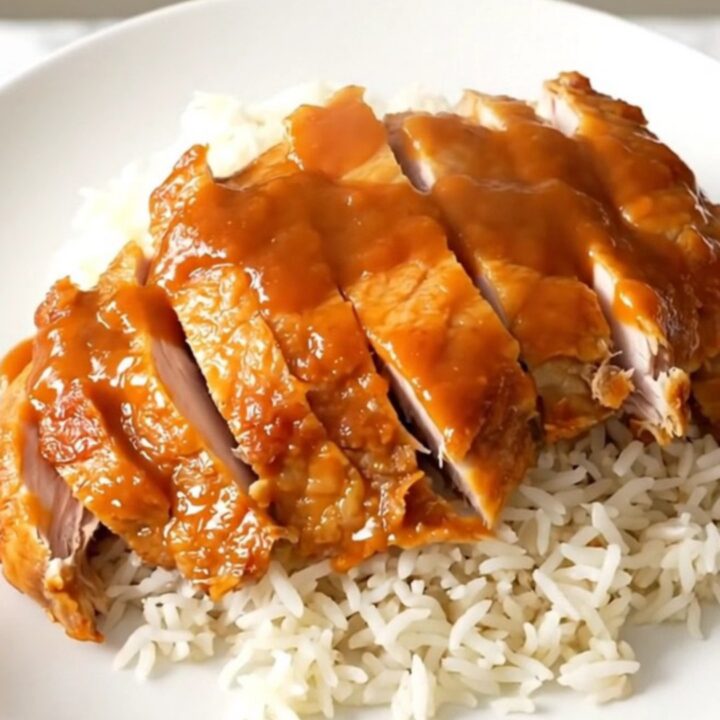 A plate of tender Chinese lemon chicken with a glossy sauce served over white rice.