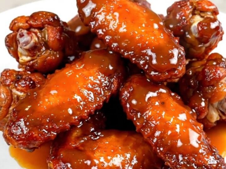 A top-down view of raw chicken wings and ingredients in a black ceramic slow cooker insert.