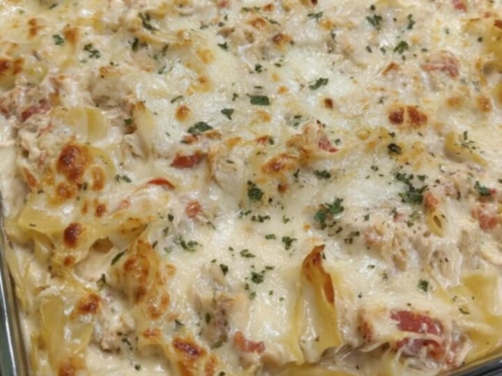 A spatula scooping a steaming, cheesy portion of chicken spaghetti lasagna bake with a long cheese pull.