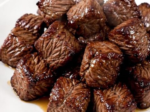 A close-up of tender, cooked steak bites and mushrooms in a slow cooker, showing a rich, savory glaze.