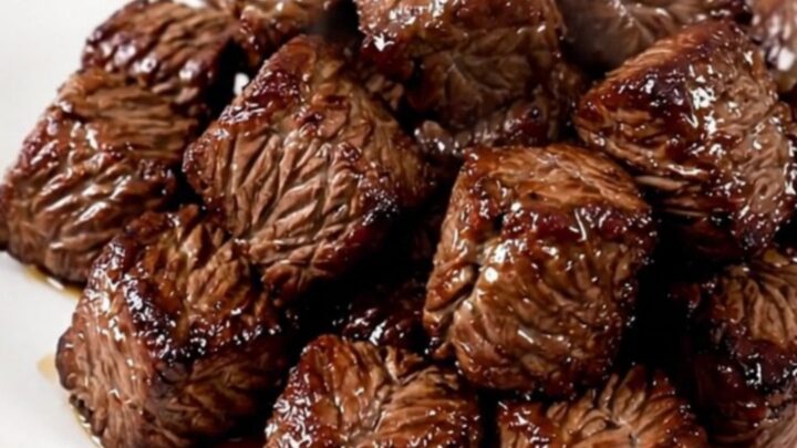 A close-up of tender, cooked steak bites and mushrooms in a slow cooker, showing a rich, savory glaze.