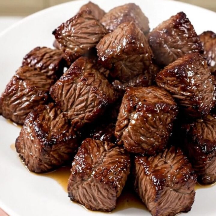 A close-up of tender, cooked steak bites and mushrooms in a slow cooker, showing a rich, savory glaze.