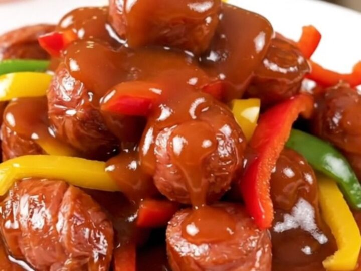 A plate of glossy, slow-cooked smoked sausage and sliced bell peppers in a sweet and sour sauce.