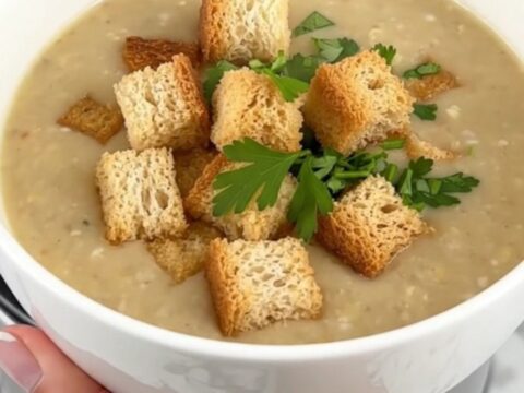 A steaming bowl of creamy potato soup garnished with golden-brown croutons and fresh green parsley.