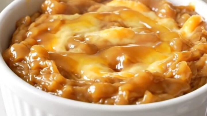 A warm, melted brie dip in a white ceramic bowl, topped with spiced apples and a drizzle of maple syrup.