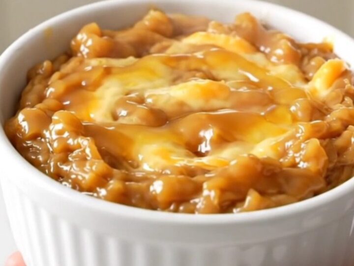 A warm, melted brie dip in a white ceramic bowl, topped with spiced apples and a drizzle of maple syrup.
