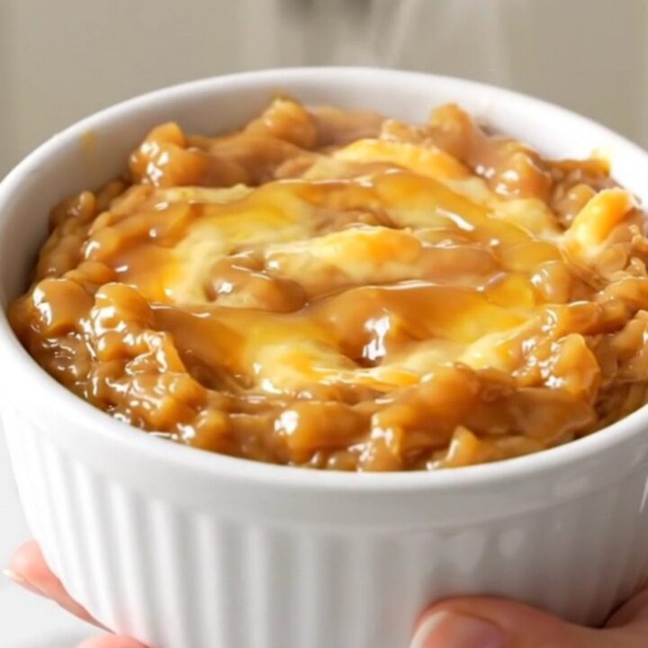 A warm, melted brie dip in a white ceramic bowl, topped with spiced apples and a drizzle of maple syrup.
