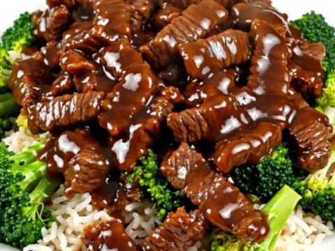 Steaming General Tso beef and tender broccoli served over white rice on a round plate.