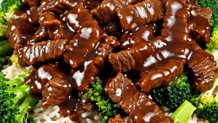Steaming General Tso beef and tender broccoli served over white rice on a round plate.
