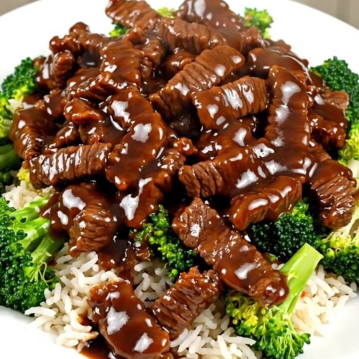 Steaming General Tso beef and tender broccoli served over white rice on a round plate.