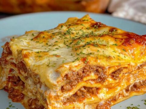A square slice of creamy Alfredo beef lasagna served on a light blue plate, showing distinct layers of seasoned beef, pasta