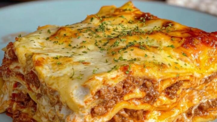 A square slice of creamy Alfredo beef lasagna served on a light blue plate, showing distinct layers of seasoned beef, pasta